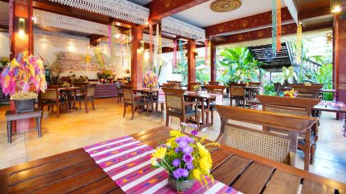 Yaang Come Village Hotel - SHA Extra Plus في شيانغ ماي: مطعم بطاولات خشبية وكراسي وزهور