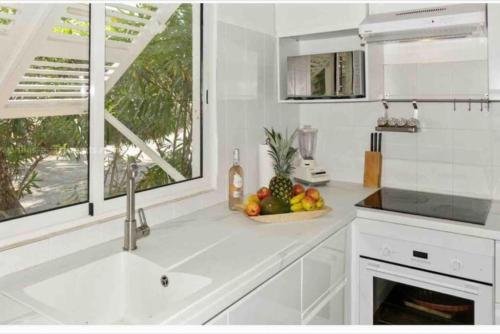 a white kitchen with a sink and a bowl of fruit at Villa Magellan, walkable Orient Bay beach, private pool in Orient Bay