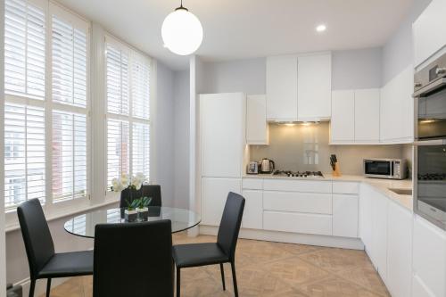 a kitchen with white cabinets and a glass table and chairs at Urban Chic - Shaftesbury in London