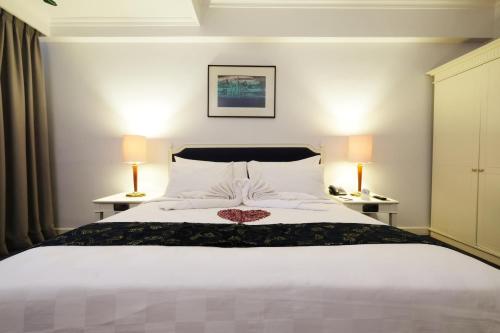 a bedroom with a large white bed with two lamps at Aryaduta Makassar in Makassar