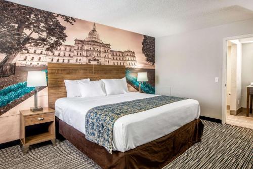 东兰辛Clarion Pointe East Lansing University Area的酒店客房设有一张大床,墙上挂有绘画作品