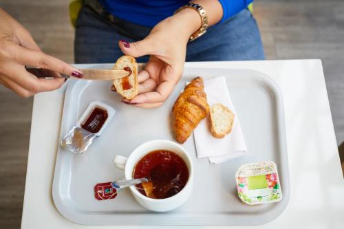 a tray with a person holding a sandwich and a cup of tea at Ibis Budget - Lille Villeneuve D'Ascq in Villeneuve d'Ascq