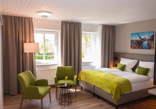 a bedroom with a bed and two green chairs at Lindenhof Hotel Garni in Sulsdorf auf Fehmarn