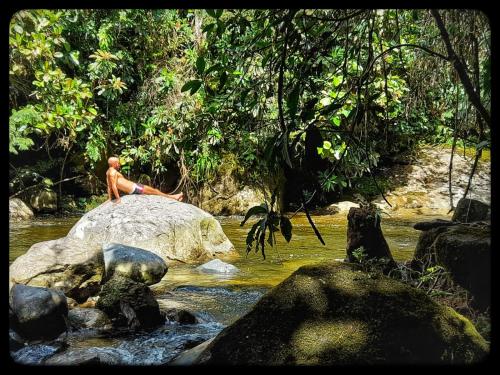 a man sitting on a rock in a river at La Perla Negra - Black Pearl Eco Hostel in San Rafael