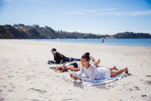 a group of people laying on towels on a beach at Waiheke Backpackers Hostel in Onetangi