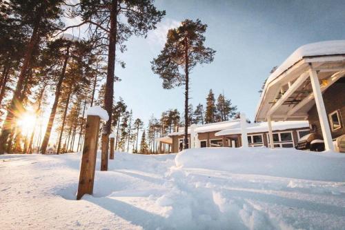 ein schneebedecktes Haus mit der Sonne im Hintergrund in der Unterkunft Chalet Norva in Rovaniemi