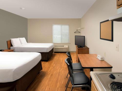a hotel room with two beds and a desk and a kitchen at WoodSpring Suites Louisville Clarksville in Clarksville