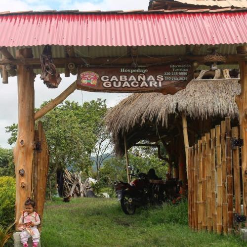 a little girl sitting in the grass next to a hut at Cabañas Guacari San Agustín huila in San Agustín