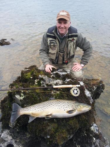 a man sitting in the water with a fish at Corrib View Lodge in Glencorrib