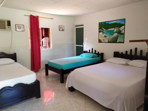 a bedroom with two beds and a red curtain at Hostal Recuerdos del Tayrona in El Zaino