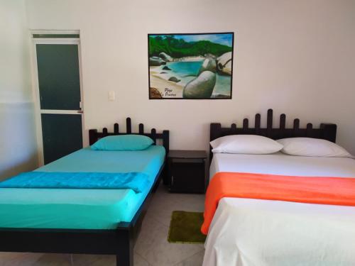 a bedroom with two beds and a picture on the wall at Hostal Recuerdos del Tayrona in El Zaino