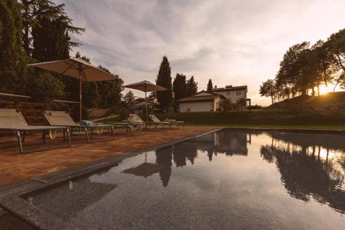 a pool with chairs and umbrellas next to a house at Borgo Le Colline Luxury Agriturismo in Tuscany in Gambassi Terme