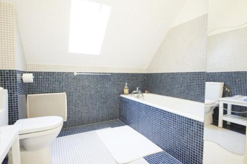 La salle de bains est pourvue de carrelage bleu, d'une baignoire et de toilettes. dans l'établissement Domaine Providence, à Lassay-sur-Croisne