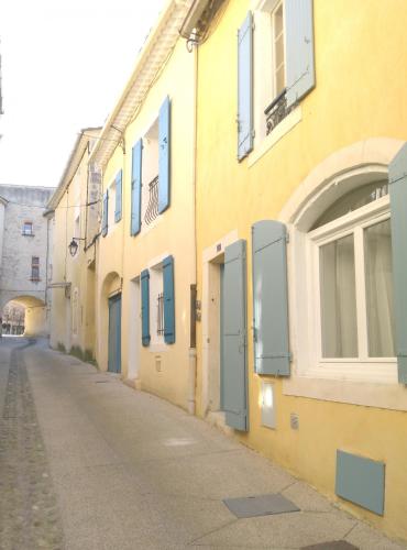 une allée vide avec un bâtiment jaune aux portes bleues dans l'établissement Appartement au coeur du village- Ref12, à Saint-Paul-Trois-Châteaux