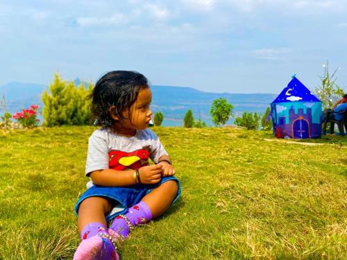 a little girl sitting on the grass in a field at Jandyal Farm House in Malshej Ghat