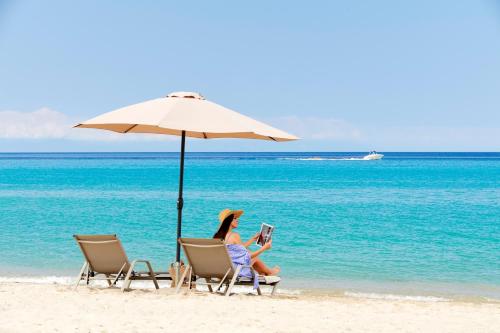 a woman sitting on a beach under an umbrella at Cavo Delea Villas & Suites in Possidi