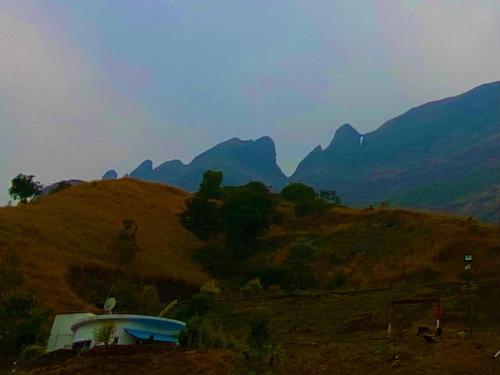 a house on a hill with mountains in the background at Jandyal Farm House in Malshej Ghat