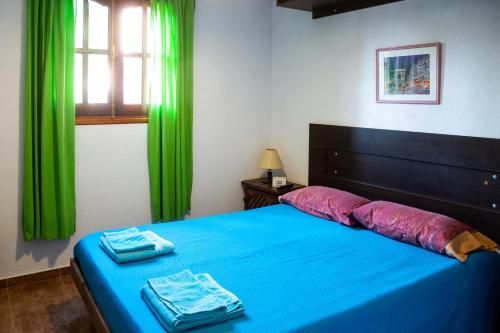 1 dormitorio con cama azul y cortinas verdes en Cabañas de la "USINA" en Cosquín