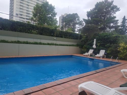 ein Pool mit zwei Stühlen und ein Gebäude in der Unterkunft Apartamento Marina de roosvelt con piscina climatizada in Punta del Este