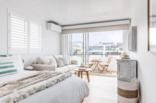 a white bedroom with a bed and a living room at The Bungalows at Bondi in Sydney