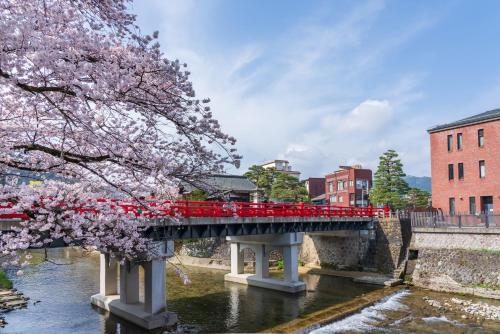 a red bridge over a river with a cherry tree at Tabist Kanko Business Hotel Matsuyama Hida Takayama in Takayama