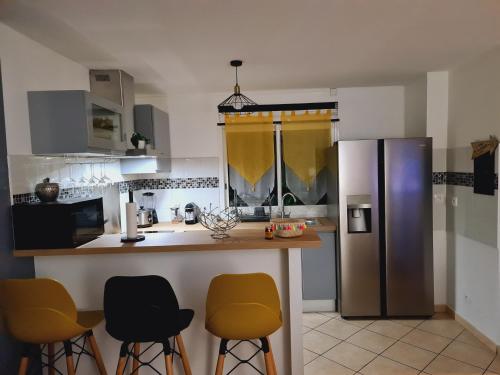 a kitchen with yellow bar stools and a stainless steel refrigerator at Le Nid Dor - Appartement de standing in Le Gosier