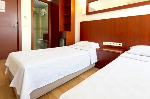 two beds in a hotel room with white sheets at Hotel Pelit in Canakkale