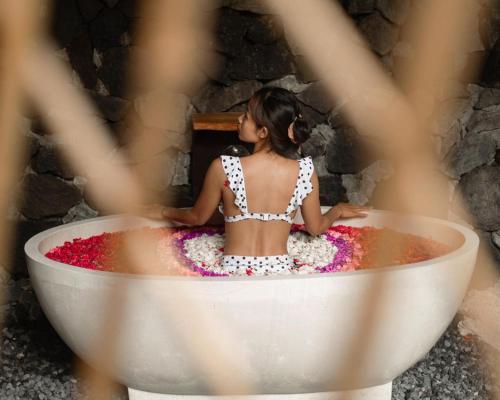 una donna seduta in una vasca da bagno piena di fiori di Sun Sang Eco Retreats a Tabanan