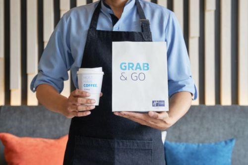a man holding a sign and a cup of coffee at Holiday Inn Express - Mülheim - Ruhr by IHG in Mülheim an der Ruhr