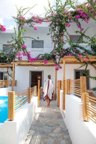 a woman walking into a building with pink flowers at Dionysos Seaside Resort Ios in Mylopotas