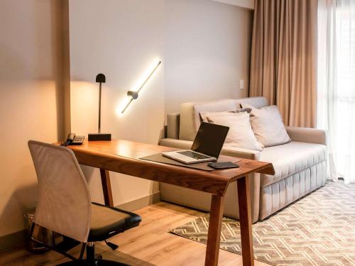 a desk with a laptop on it in a room with a couch at Mercure Curitiba Batel in Curitiba