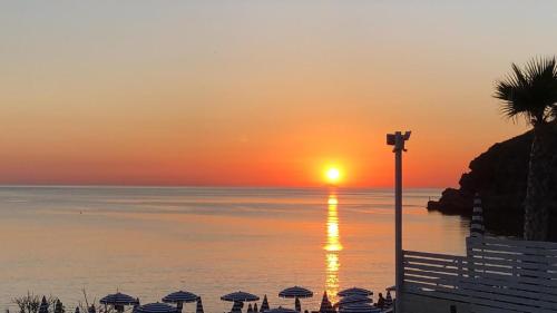 a sunset over the ocean with umbrellas and a street light at Toscana Charme Resort in Tirrenia