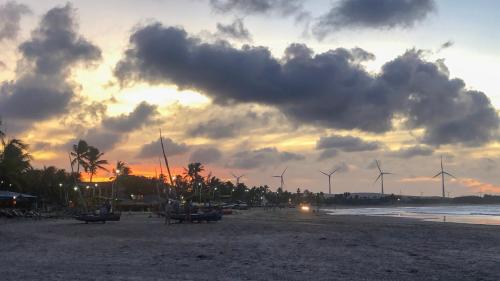 a sunset on a beach with windmills in the background at Bella Spiaggia Suítes in Flecheiras