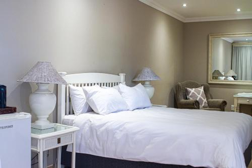 a bedroom with a white bed and a chair and a mirror at Machauka Lodge in Lephalale