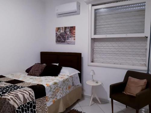 um quarto com uma cama, uma cadeira e uma janela em Apartamento Alto padrão de Frente para o mar no Guarujá