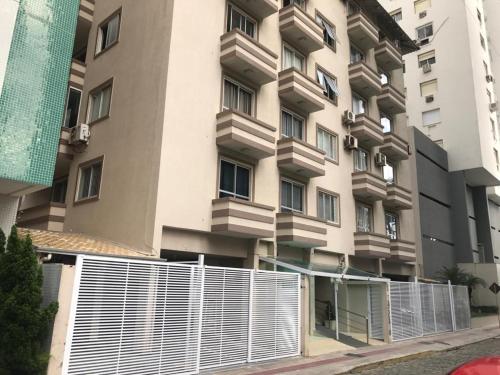 un edificio con una valla blanca delante de él en Apartamento Balneário Camboriú - 2 quartos 80m do mar, en Balneário Camboriú