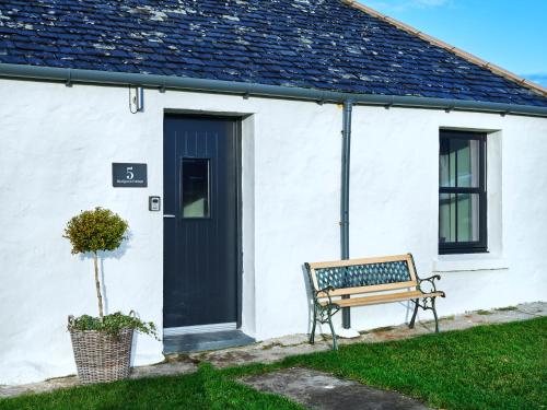 Eine Bank vor einem weißen Haus mit schwarzer Tür in der Unterkunft Monkstadt Room 21 - MacQueen Cottage in Portree