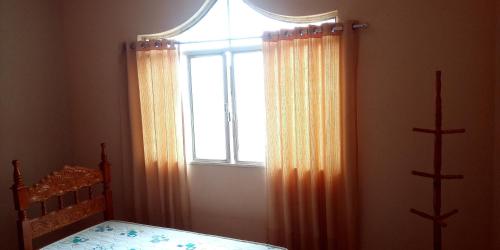 a bedroom with a bed and a window with curtains at Hostel e Pousada Solar in Poços de Caldas