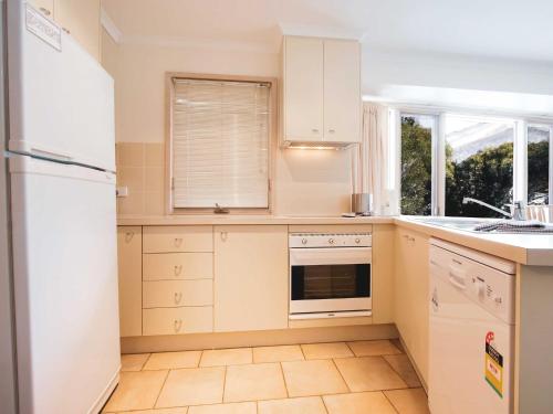 a kitchen with white cabinets and a white refrigerator at Lhotsky 1 Bedroom apartment with tranquil outlook and onsite parking in Thredbo