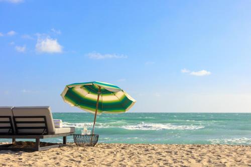 a beach with a chair and an umbrella on the sand at Kimpton Surfcomber Hotel by IHG in Miami Beach
