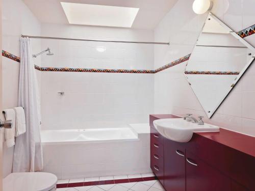 La salle de bains est pourvue d'une baignoire, d'un lavabo et d'un miroir. dans l'établissement Village Green 2 Bedroom loft townhouse with views fireplace and garage parking, à Thredbo