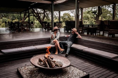 two people sitting on a bench next to a fire pit at Honeyguide Tented Safari Camp - Khoka Moya in Manyeleti Game Reserve
