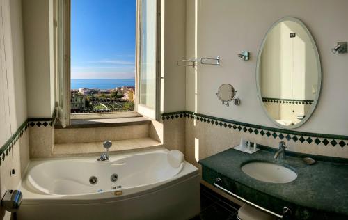 ein Badezimmer mit einer Badewanne, einem Waschbecken und einem Spiegel in der Unterkunft Miglio d'Oro Park Hotel in Ercolano