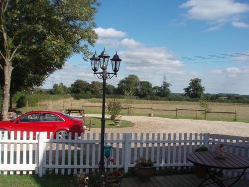 a white fence with a street light next to a red car at Meadow Farm Cottage in Norwich