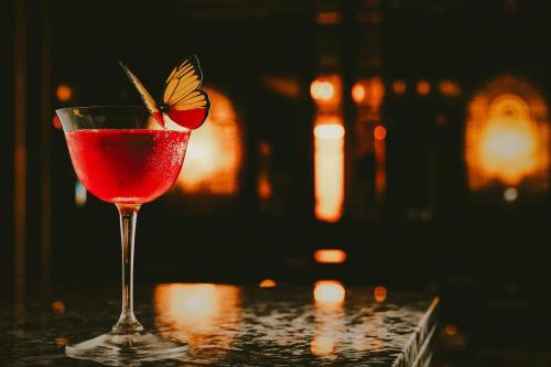 a red drink in a glass with a butterfly on it at The Mayfair Townhouse - an Iconic Luxury Hotel in London