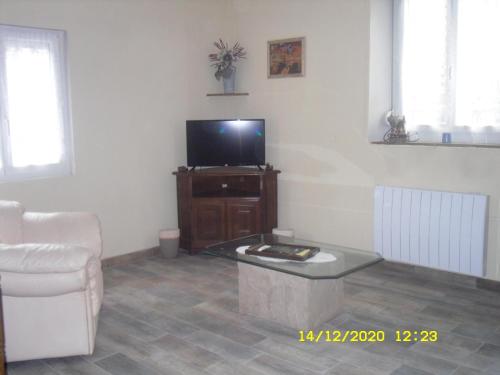 ein Wohnzimmer mit einem TV, einem Sofa und einem Tisch in der Unterkunft Maison - Chambre d’hôte située au cœur d Asfeld in Asfeld