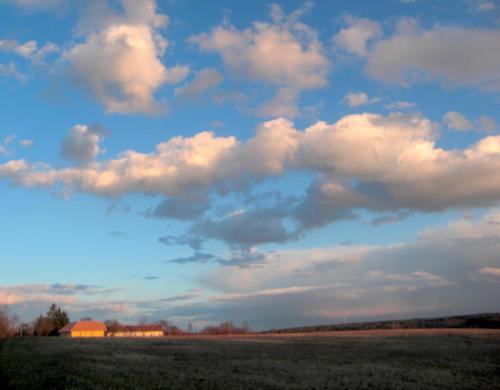a field with a cloudy sky and a house at Naturpark Ferienhaus in Szalafő