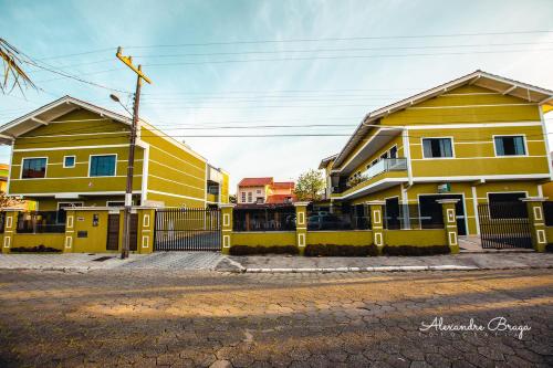 two yellow houses with a fence on a street at ApartPousada Residencial dos Reis in São Francisco do Sul