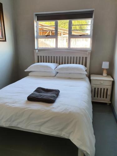 a bedroom with a white bed with a window at Volgenoeg Self Catering in Oudtshoorn