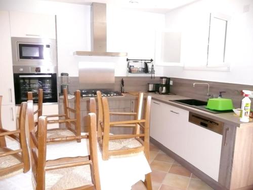 - une cuisine avec des placards blancs et des chaises en bois dans l'établissement Appartement charmant à Sainte Croix du Verdon avec terrasse, à Sainte-Croix-de-Verdon